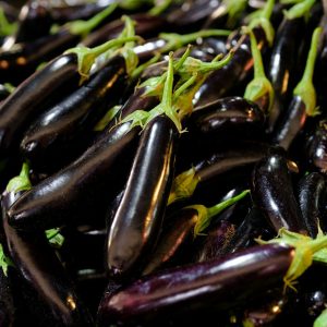 a pile of purple eggplant with green stems